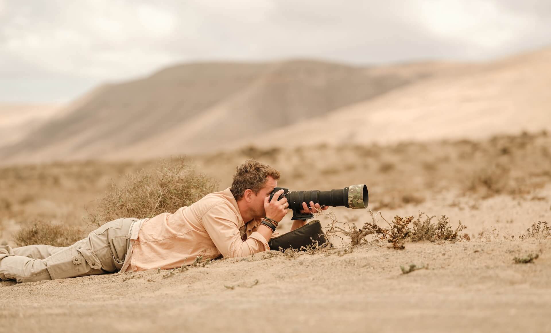 Photographer lying in arid terrain with telephoto lens capturing mountain landscape in the Canary Islands.