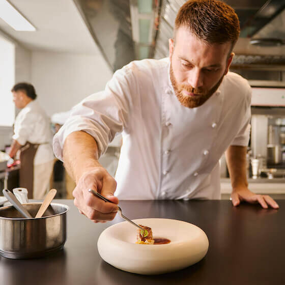 Chef delicately placing an ingredient on a gourmet dish in a professional kitchen.