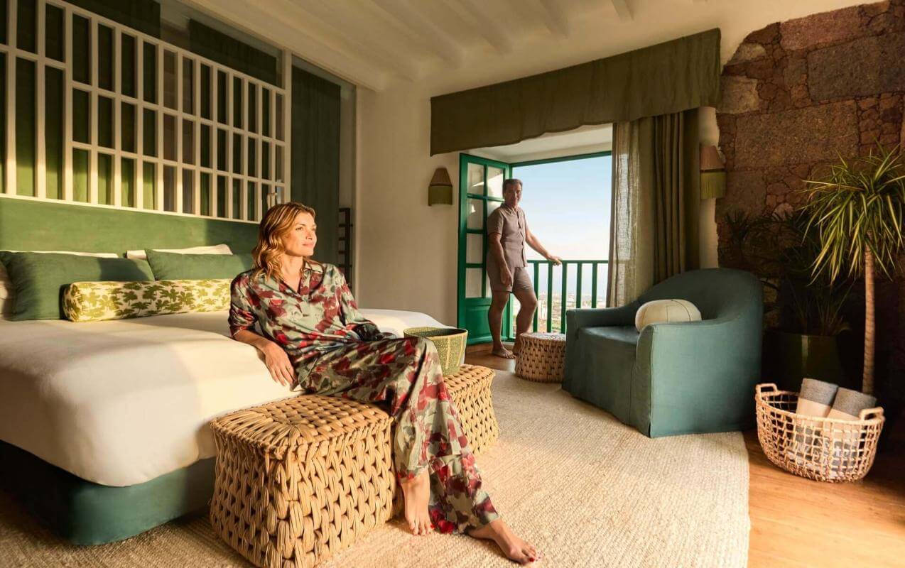 Person relaxing in a room decorated in shades of green with a terrace opening out onto the scenery, in a warm, welcoming atmosphere.