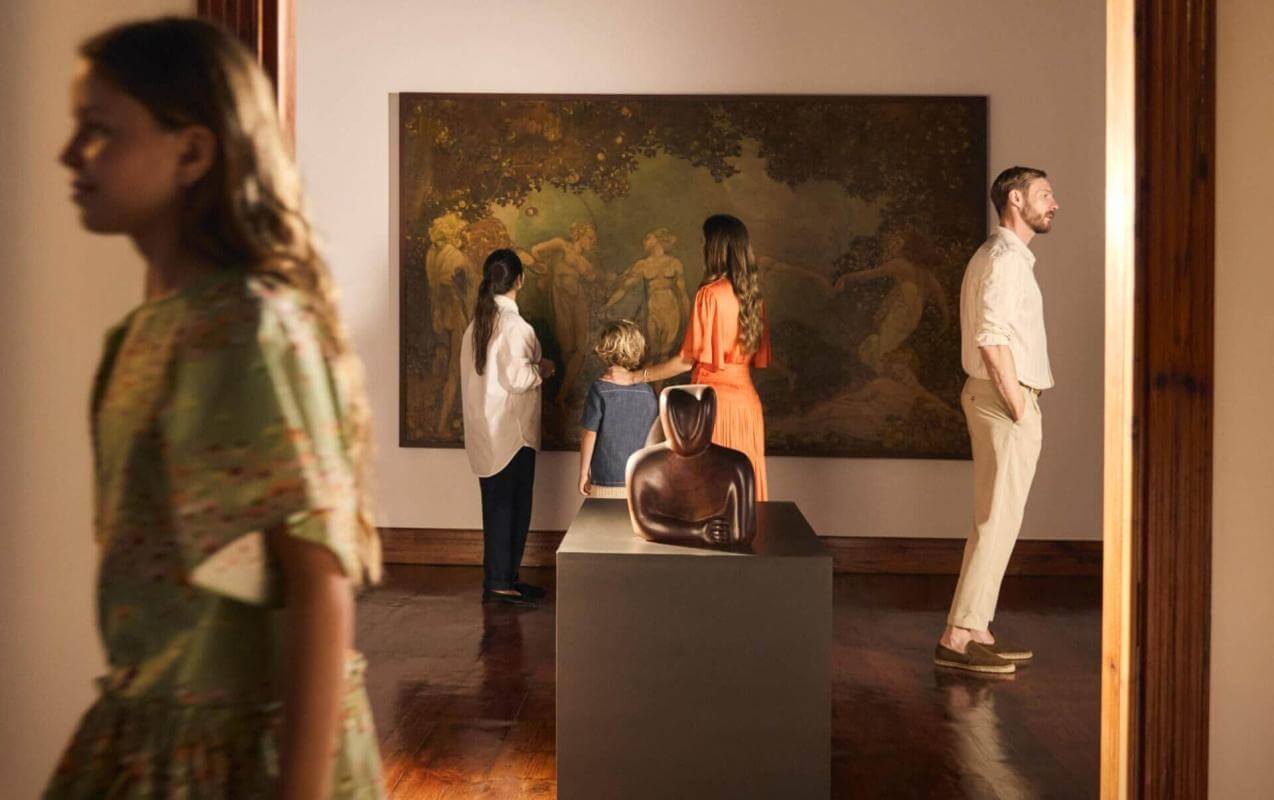 Group visiting an art exhibition in a museum with large paintings and sculptures in a brightly lit room.