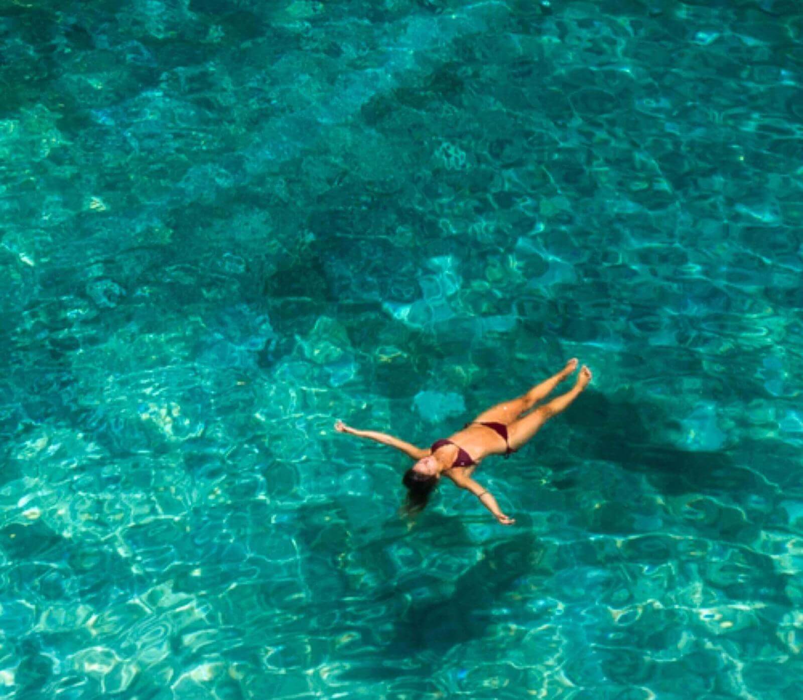 Person floating relaxed in clear turquoise waters.