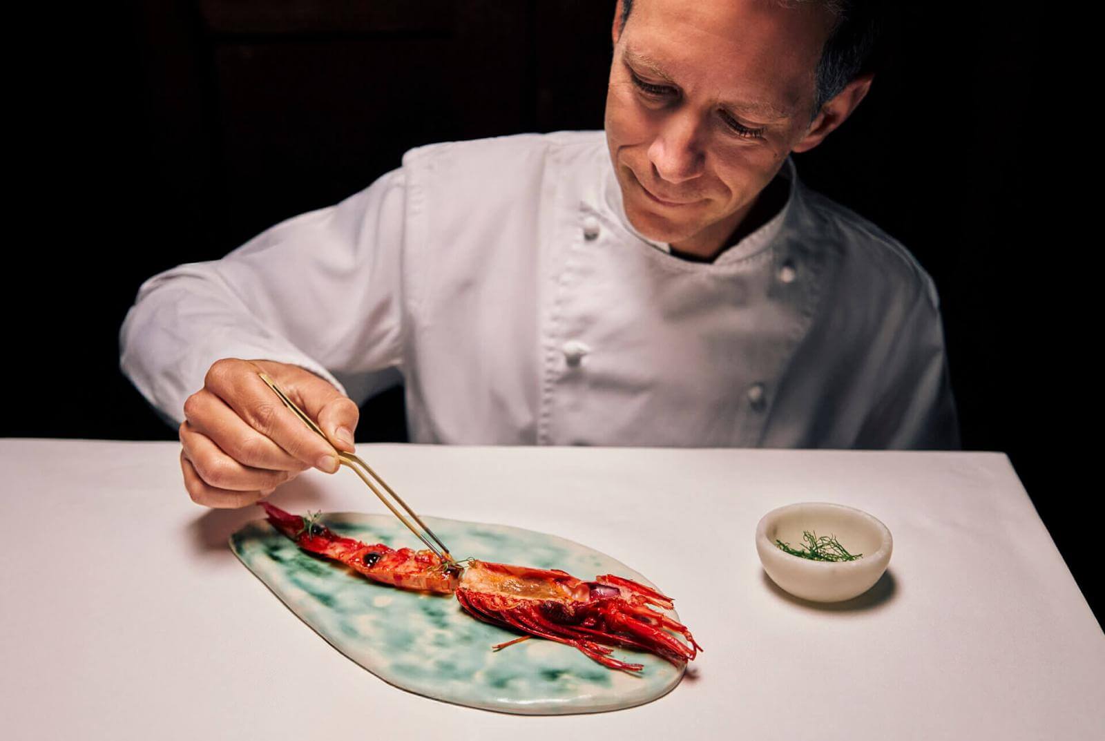 Chef delicately placing a cardinal prawn on artistic tableware with turquoise hues.