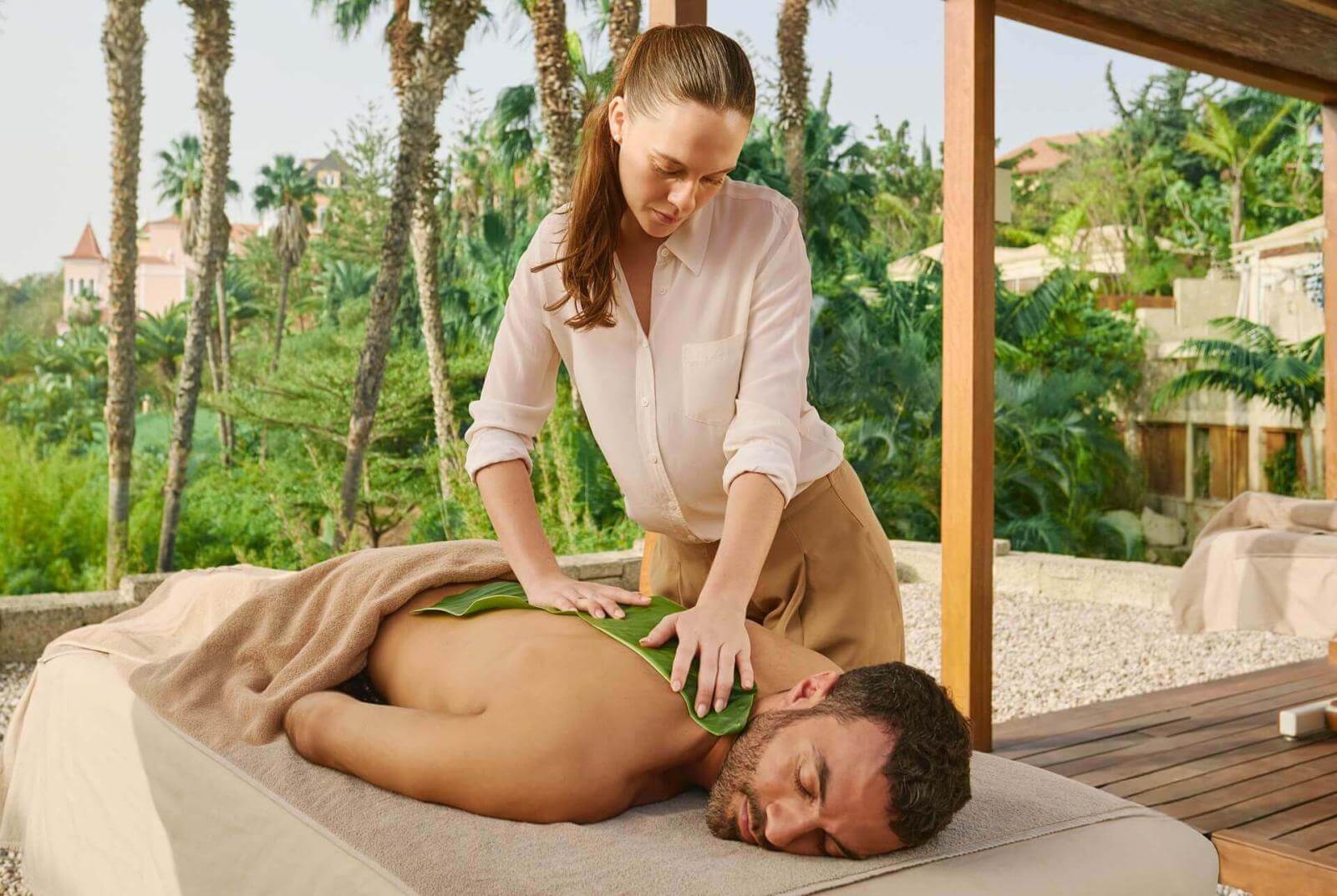 Therapist performing aloe treatment outdoors, surrounded by palm trees.