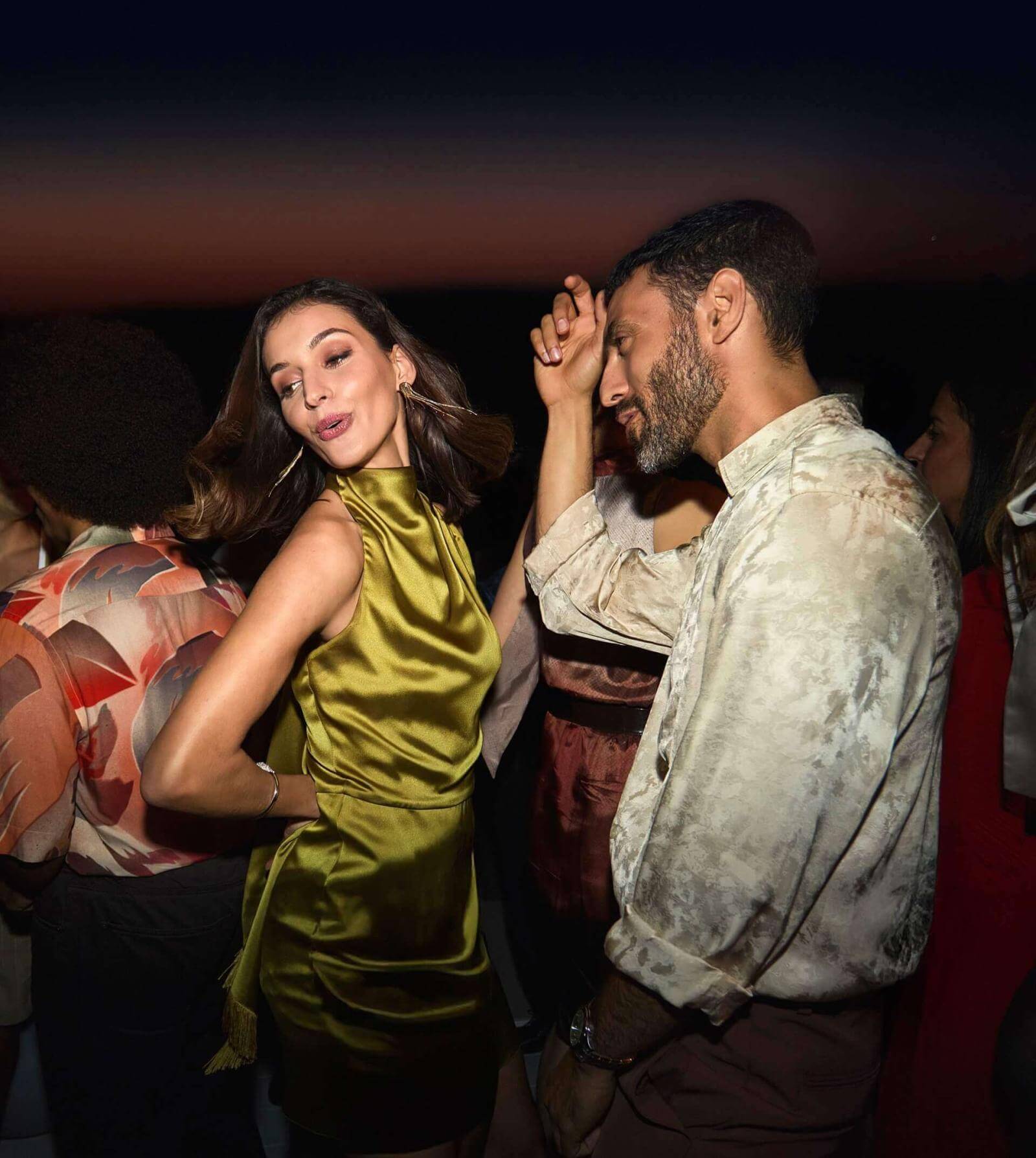 Couple dancing on rooftop terrace overlooking the sea at dusk.