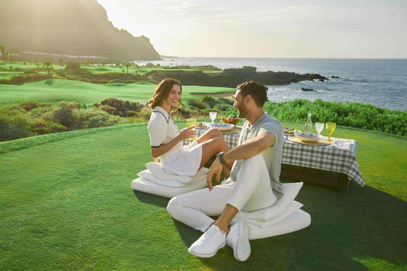 Couple enjoying a picnic with a set table on a golf course overlooking the ocean and mountains in the Canary Islands.