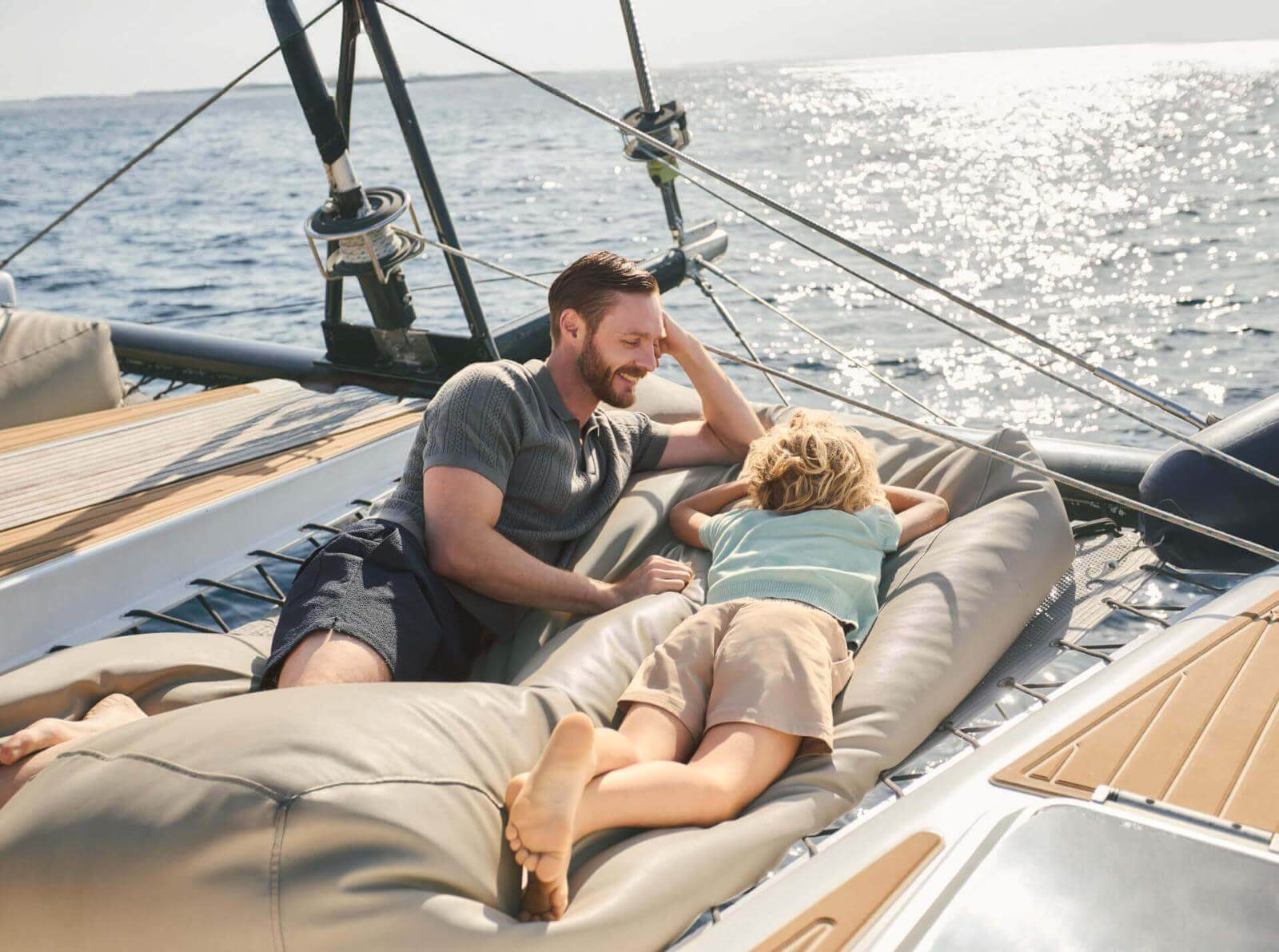 Two people relaxing on airbeds on the deck of a sailing boat at sea.