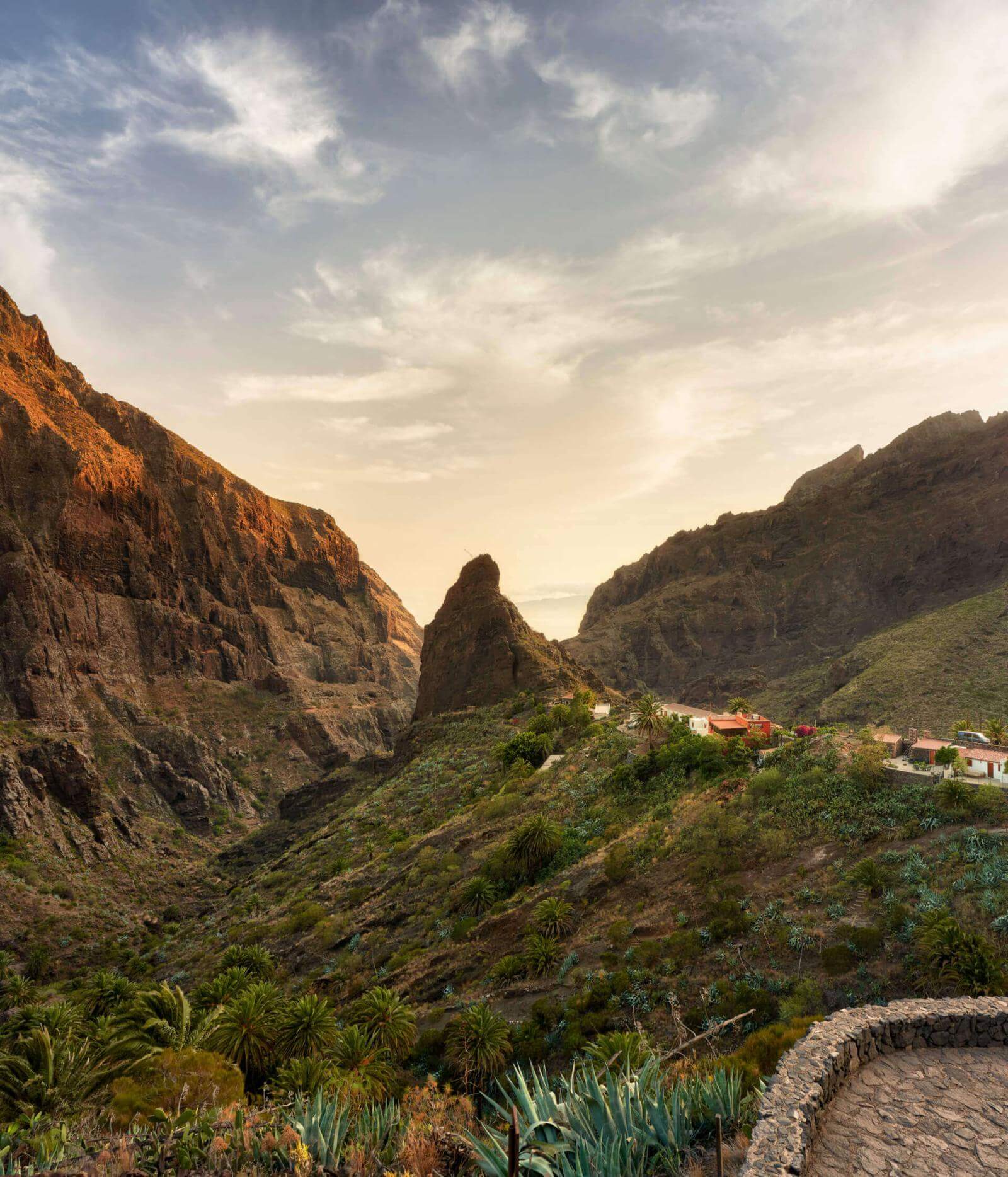 Rocky cliffs in a valley with vegetation and houses on the slopes, illuminated by the soft light of dusk.