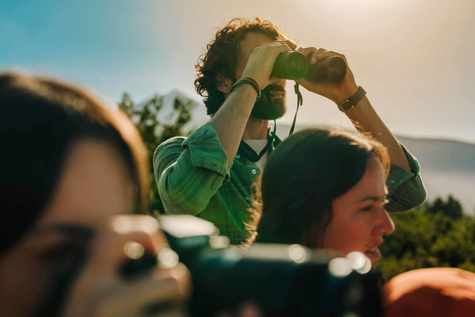 A group observes the scenery with one person using binoculars and another holding a camera in the foreground.