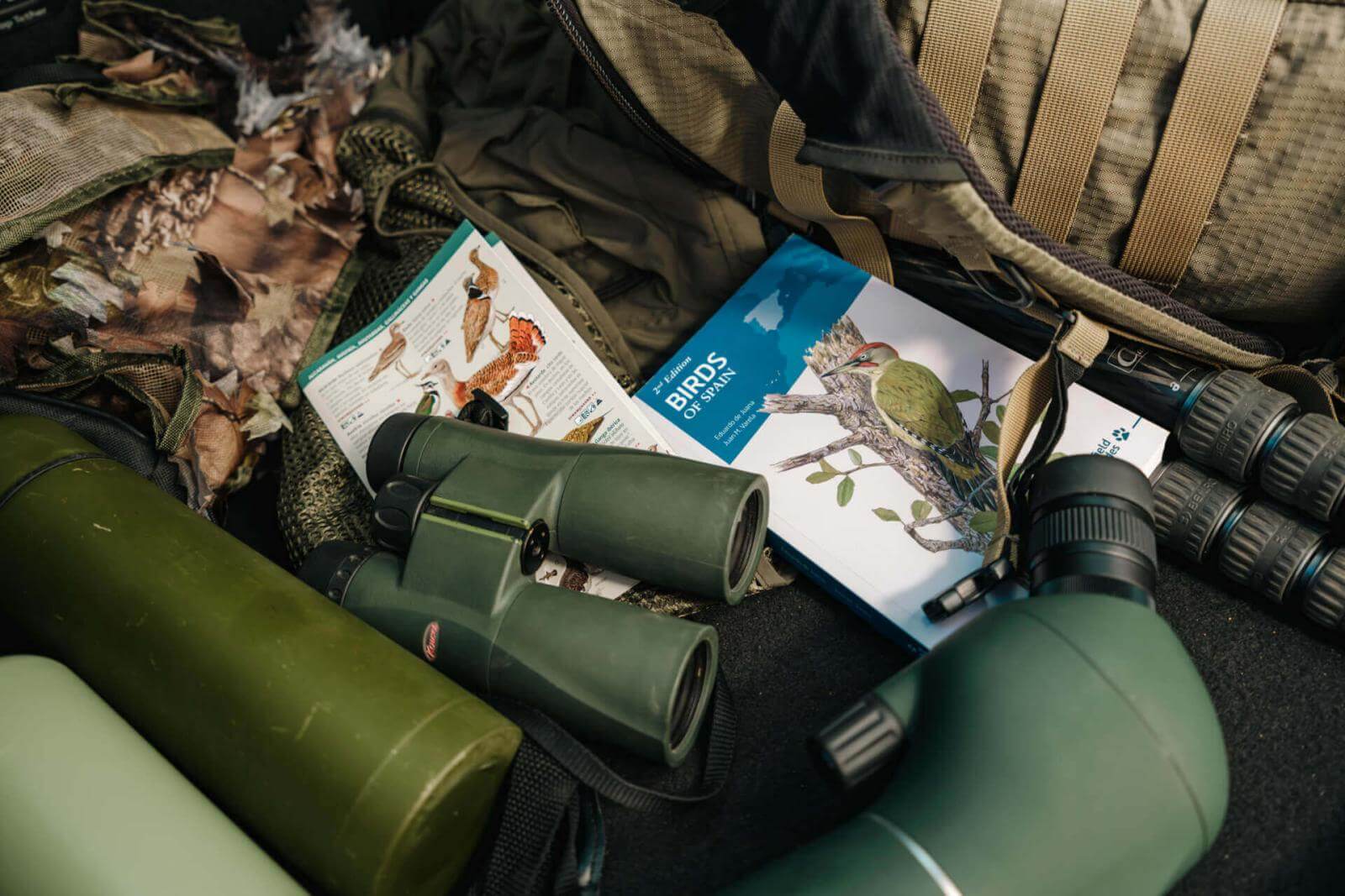 Birdwatching equipment: binoculars, terrestrial telescope, illustrated guide books and camouflage backpack.