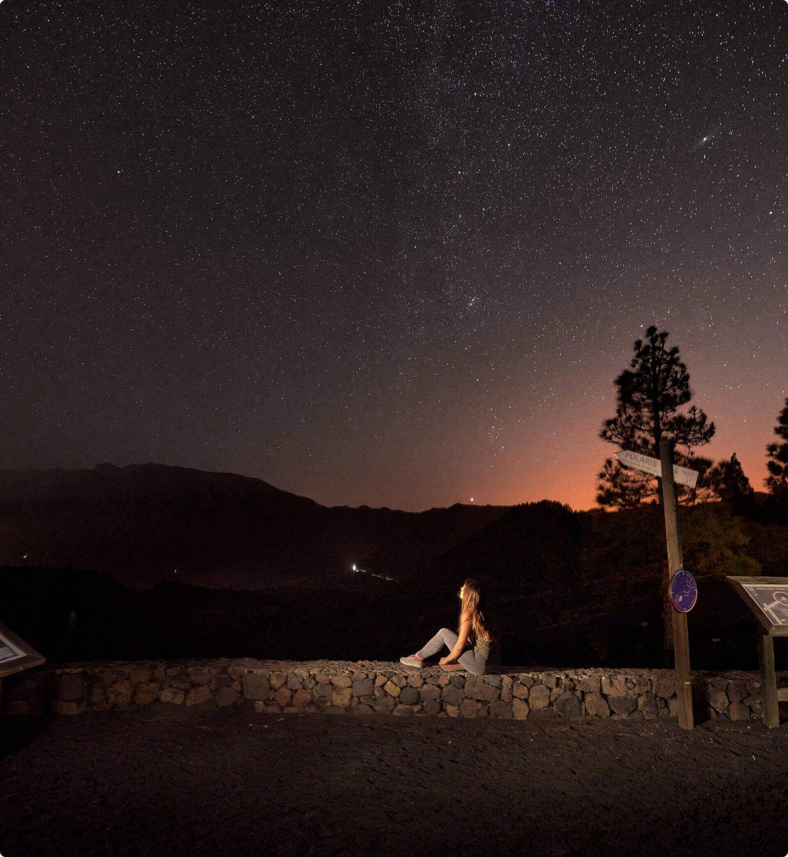 Starry night at Llano del Jable viewpoint, La Palma, with mountain silhouettes and person viewing the scenery.