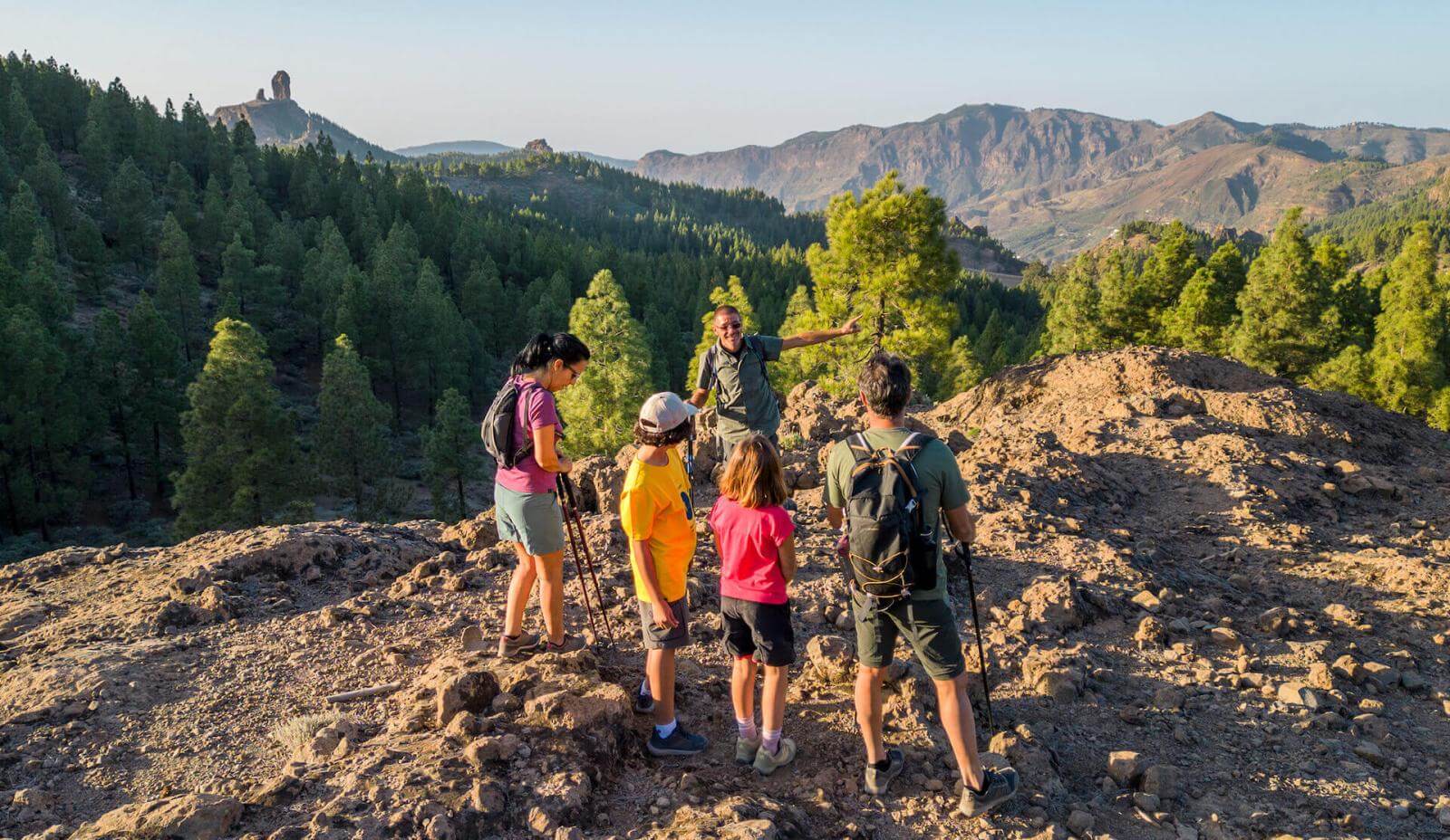 Group hike through the Roque Nublo Rural Park, amid rocky ground, Canary pine forest, and the peak beyond.