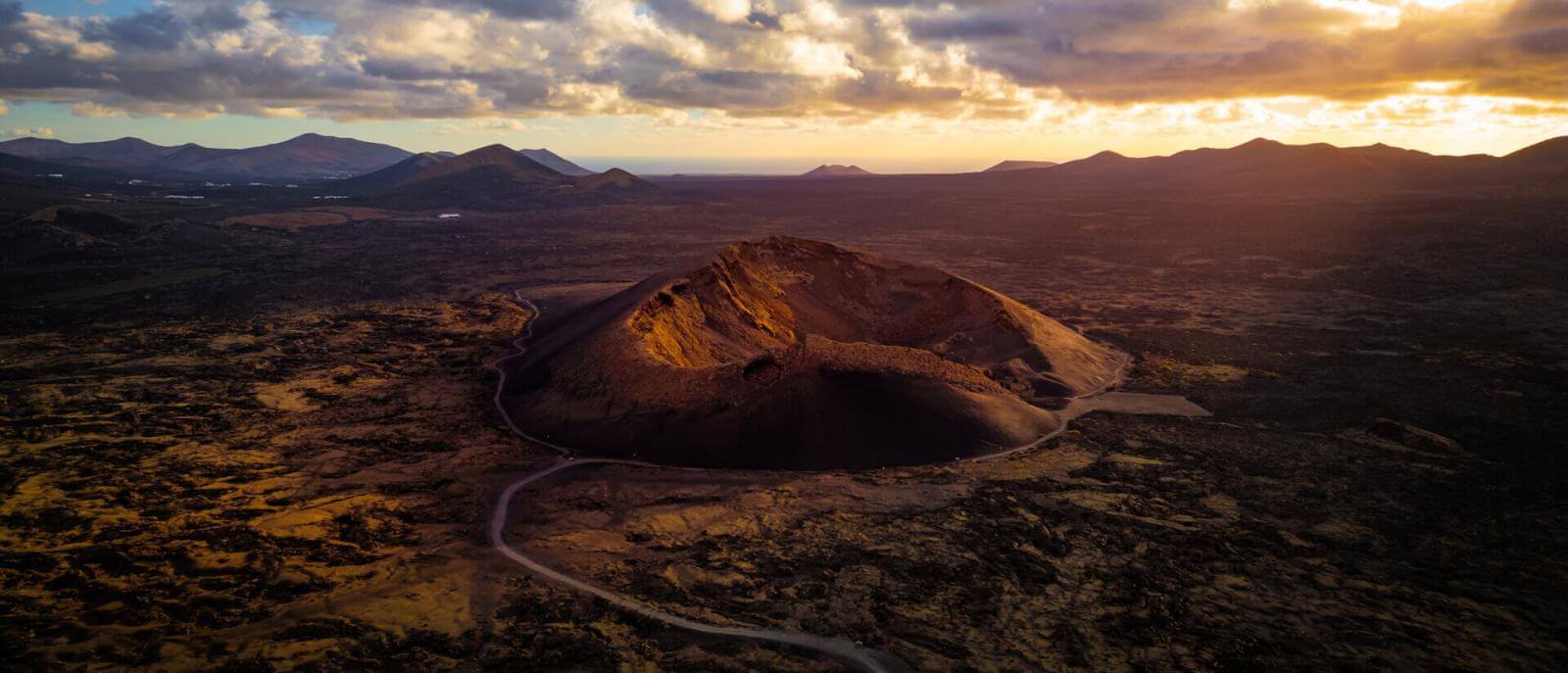 Aerial view of Lanzarote’s Cuervo Volcano at dusk, its crater illuminated against the volcanic landscape.