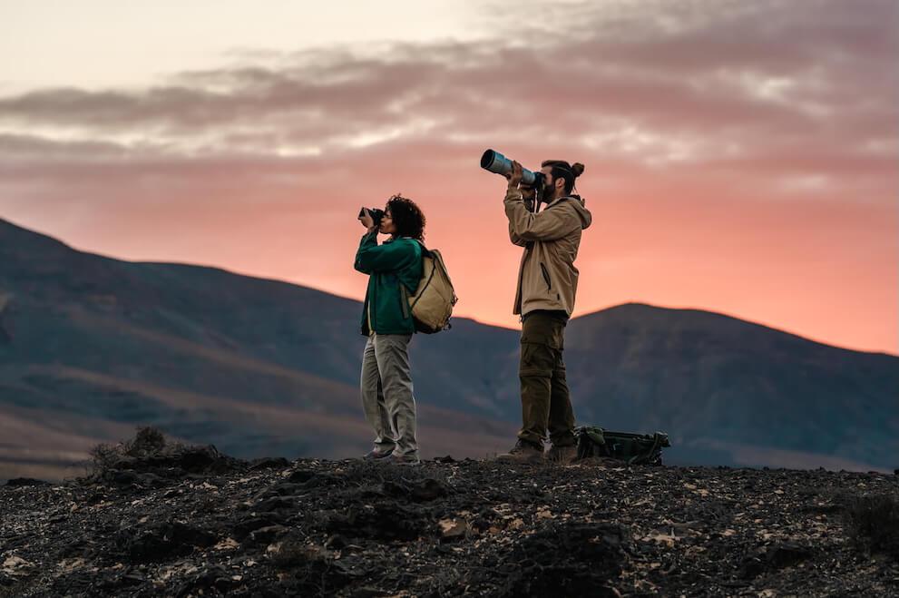 Two birdwatchers with binoculars and telephoto lens in volcanic landscape at dawn, Canary Islands.