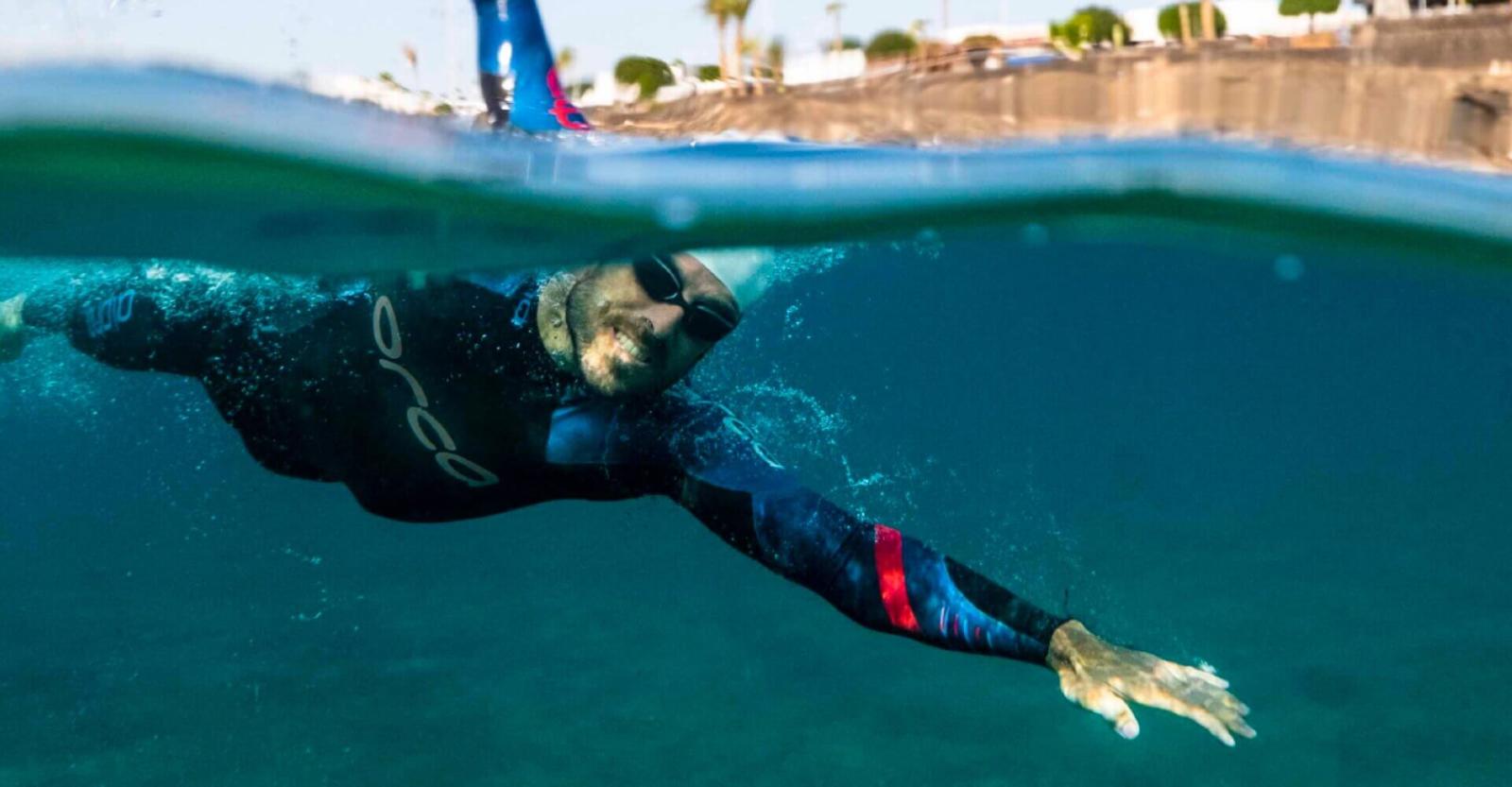 Person swimming in open water wearing a wetsuit.