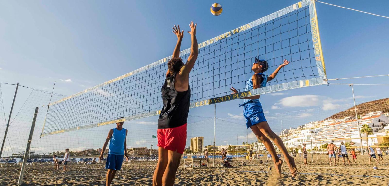 People playing beach volleyball, jumping to contest the ball.