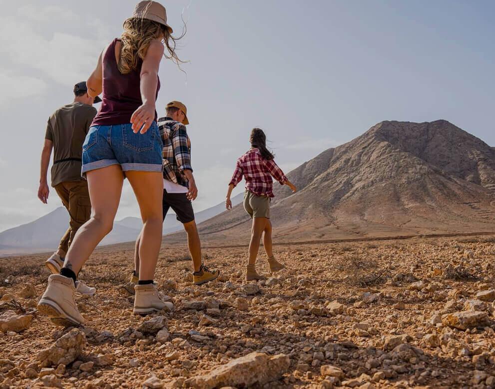 A group walking through arid terrain towards a mountain in a wide-open natural landscape.