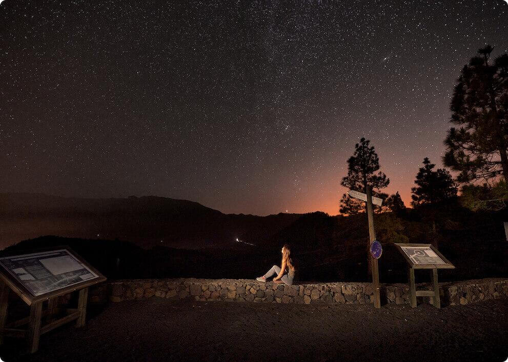 Starry night at Llano del Jable viewpoint, La Palma, with mountain silhouettes and person viewing the scenery.