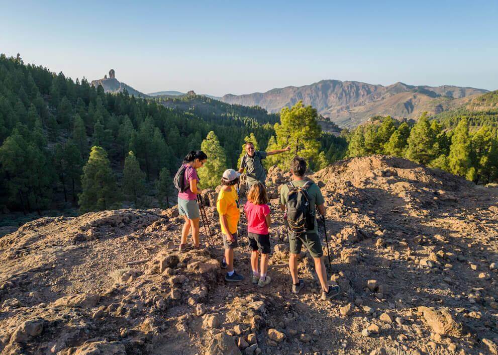 Group hike through the Roque Nublo Rural Park, amid rocky ground, Canary pine forest, and the peak beyond.
