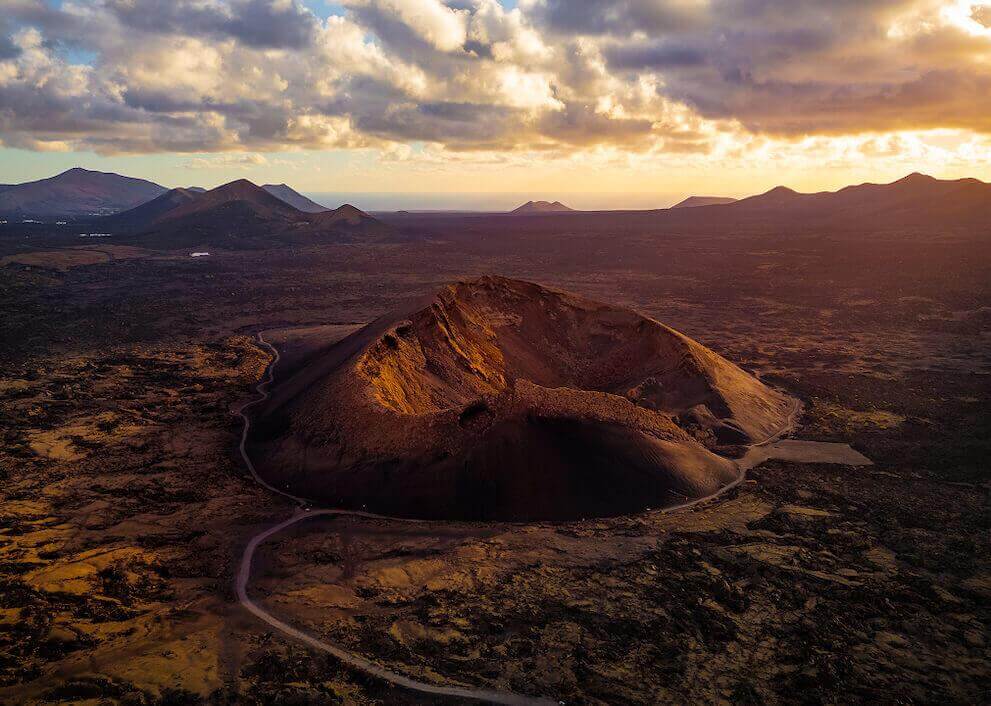 Aerial view of Lanzarote’s Cuervo Volcano at dusk, its crater illuminated against the volcanic landscape.