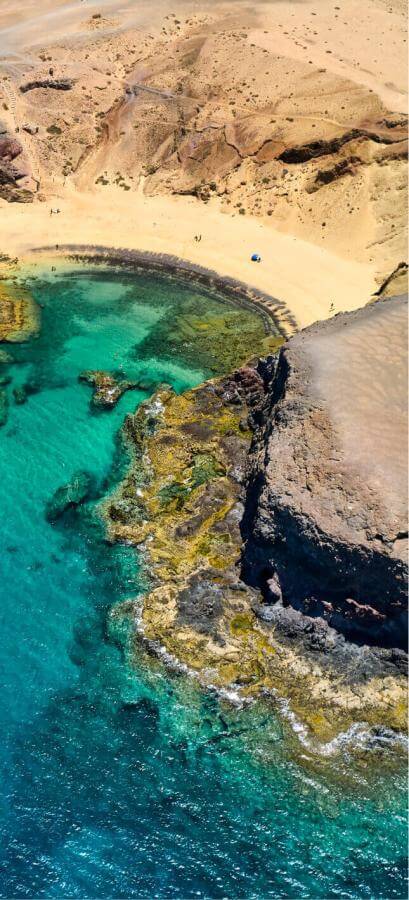 Aerial view of Papagayo beach, Lanzarote: golden sand, volcanic cliffs, and turquoise sea.