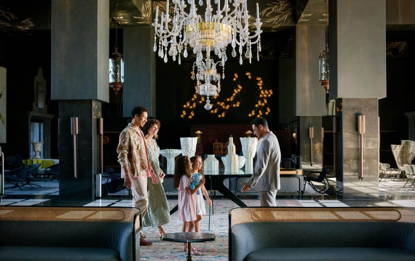 Family arriving at an elegant hotel with a crystal chandelier and sophisticated furnishings, in a spacious area with contemporary design.