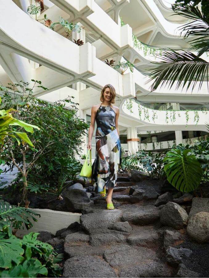 Person walking along a path surrounded by tropical vegetation in an interior with white architecture and organic design.