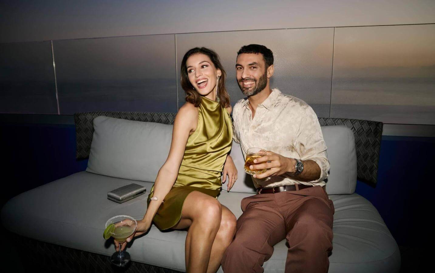 Couple enjoying cocktails on a terrace at sunset with sea views and an elegant atmosphere.