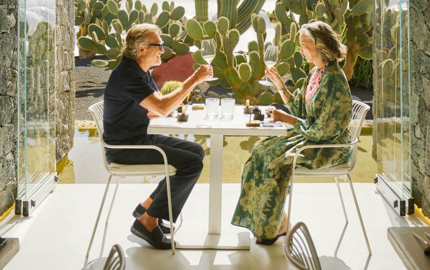 Two people enjoying food in front of the door of a bright terrace surrounded by cacti, in a modern, welcoming space.