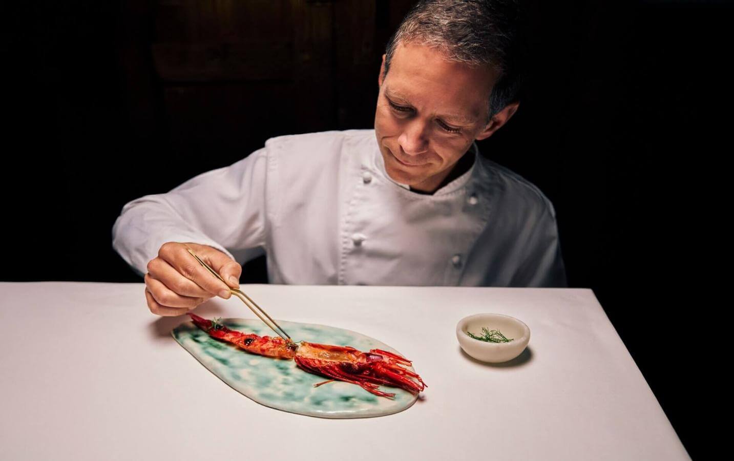 Chef placing seafood on a gourmet plate in a professional kitchen, showcasing culinary technique and haute cuisine.
