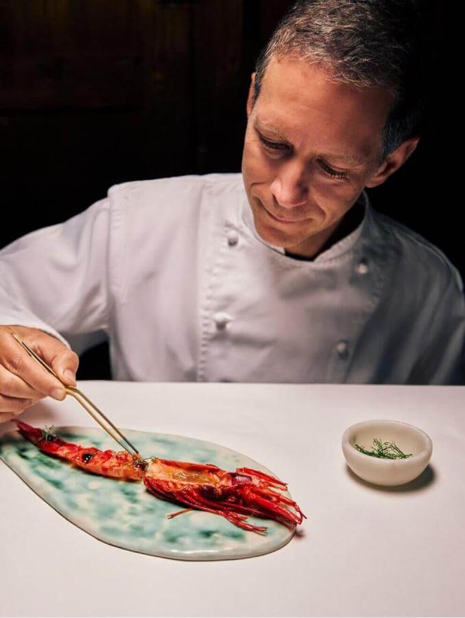 Chef placing seafood on a gourmet plate in a professional kitchen, showcasing culinary technique and haute cuisine.