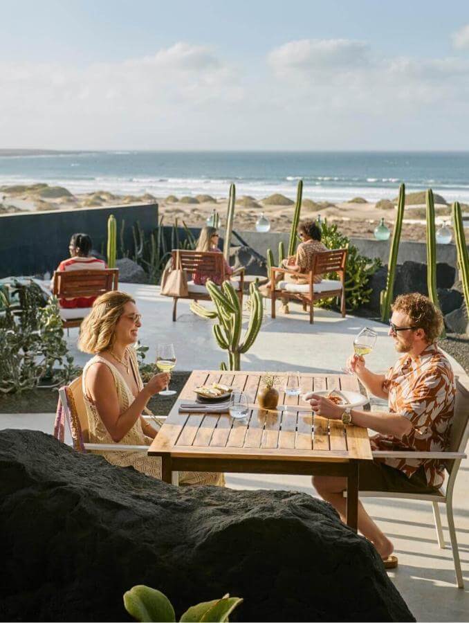 People sharing a meal on a terrace overlooking the sea, surrounded by cacti and furniture with a contemporary design.