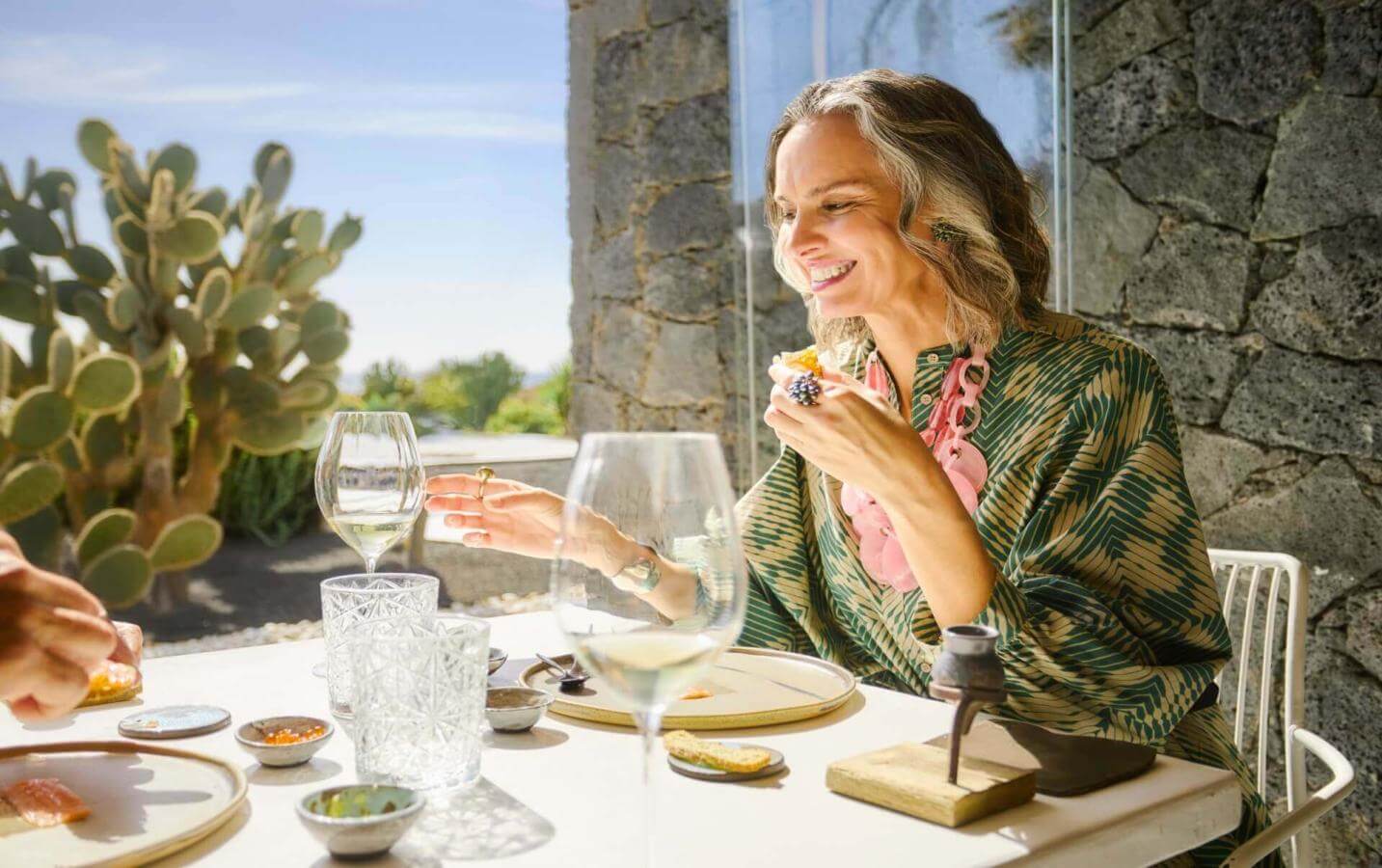 Person enjoying a meal at an outdoor table with elegant tableware, surrounded by cacti and natural light.