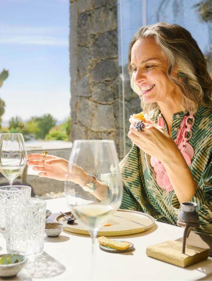 Person enjoying a meal at an outdoor table with elegant tableware, surrounded by cacti and natural light.